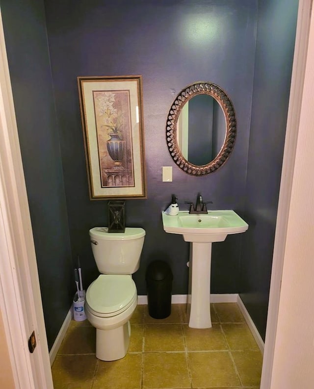 half bathroom featuring toilet, a sink, tile patterned floors, and baseboards