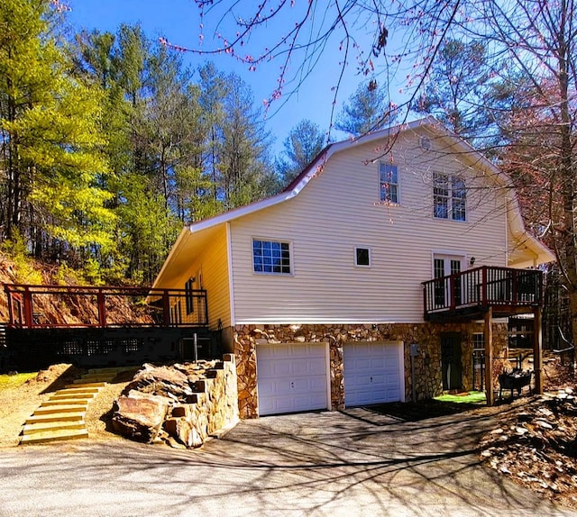 view of side of property featuring concrete driveway, a wooden deck, stone siding, and a garage