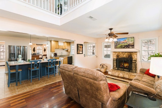 living room featuring a fireplace, a ceiling fan, visible vents, and dark wood finished floors