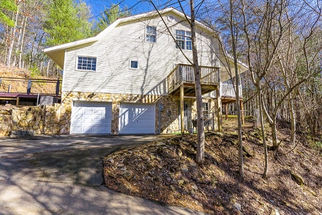view of front of property with driveway, a wooden deck, an attached garage, and stone siding