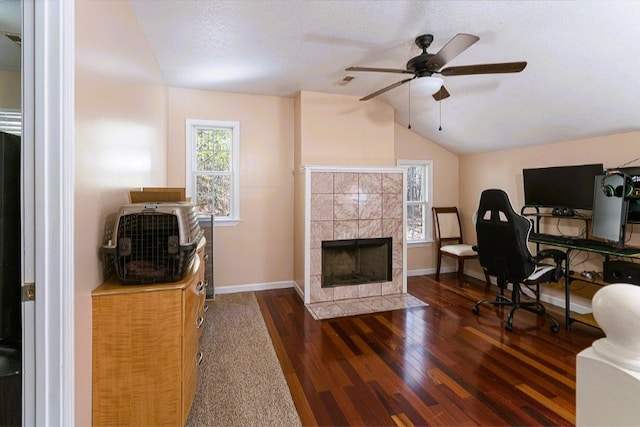 office with lofted ceiling, ceiling fan, baseboards, wood finished floors, and a tiled fireplace
