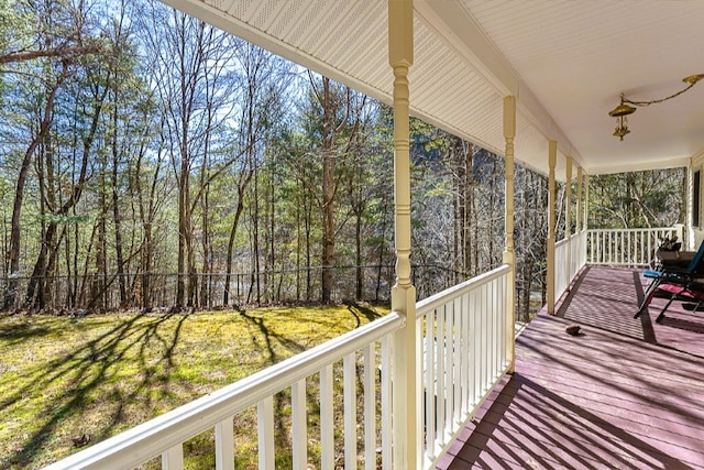 wooden terrace with covered porch, fence, a wooded view, and a yard