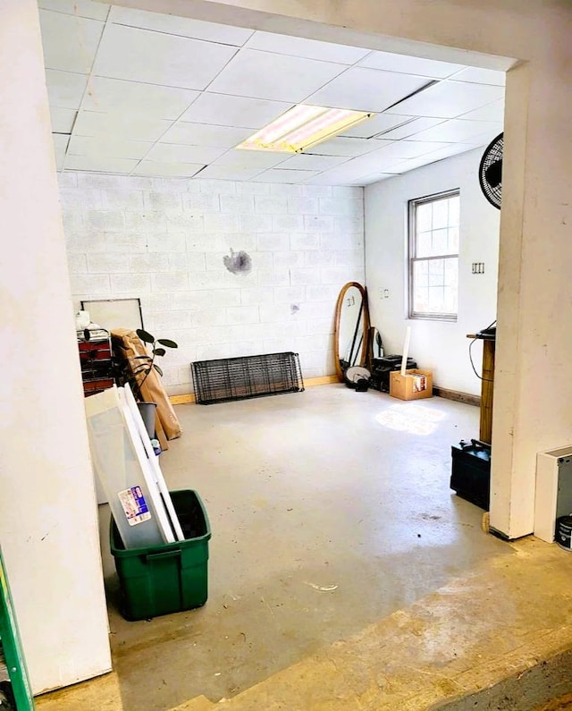 basement featuring concrete block wall and a drop ceiling