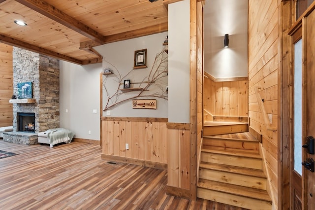 interior space with a stone fireplace, beamed ceiling, wooden ceiling, and wood finished floors