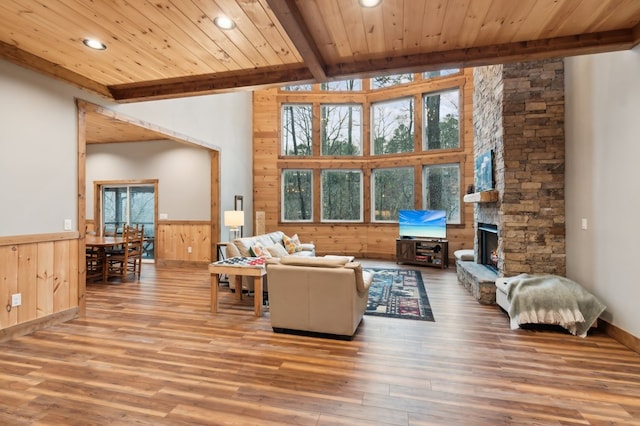 living room with wood ceiling, a stone fireplace, beam ceiling, and wainscoting