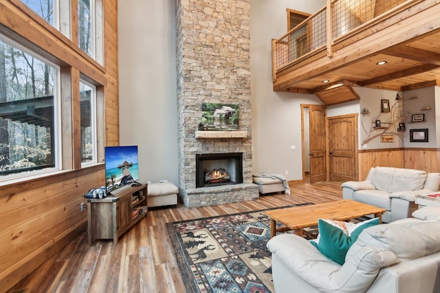 living area featuring a stone fireplace, a wainscoted wall, wood walls, wood finished floors, and a towering ceiling