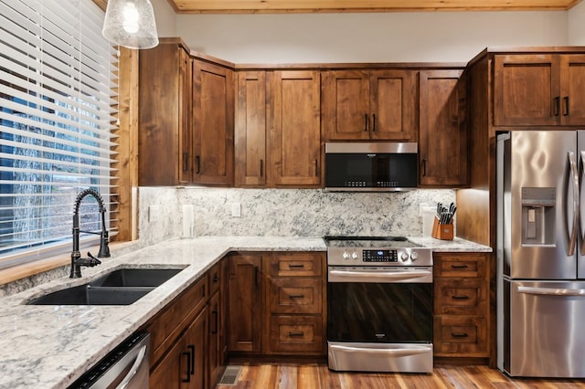 kitchen with light stone counters, stainless steel appliances, a sink, light wood-style floors, and decorative backsplash