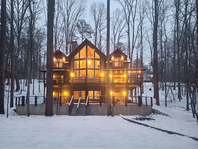 snow covered property with stairway, a chimney, and a balcony