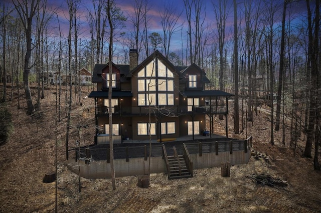 back of house at dusk with a chimney and stairs