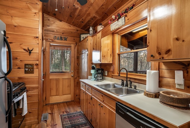 kitchen with wooden ceiling, wooden walls, stainless steel appliances, a sink, and light countertops