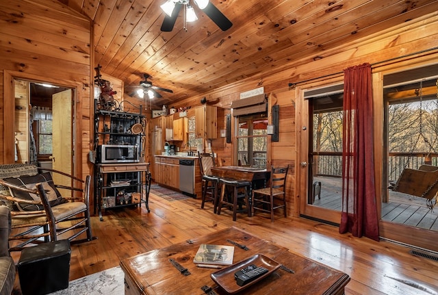 living area featuring light wood finished floors, visible vents, a ceiling fan, wooden ceiling, and wood walls