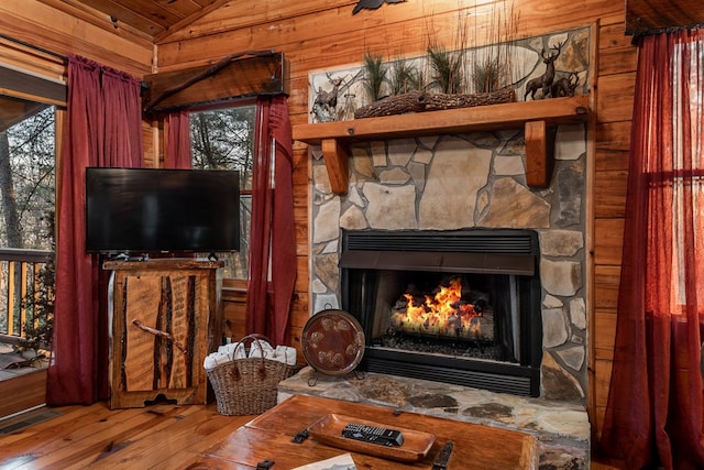 living area featuring visible vents, hardwood / wood-style flooring, vaulted ceiling, wood walls, and a fireplace