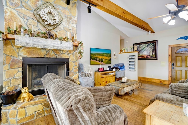 living area with a ceiling fan, wood finished floors, a stone fireplace, baseboards, and lofted ceiling with beams