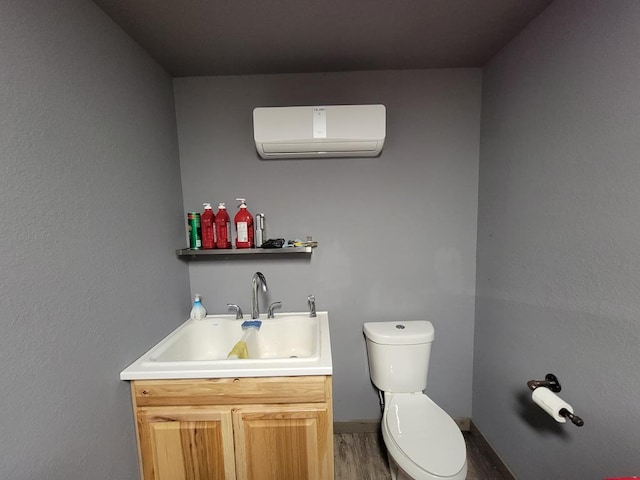 bathroom featuring a wall mounted AC, wood finished floors, vanity, baseboards, and toilet