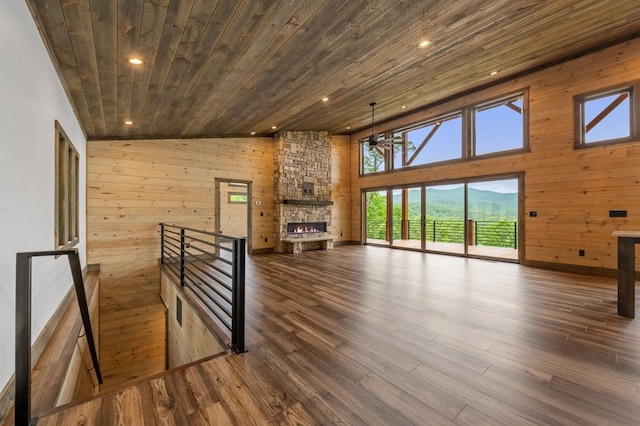 unfurnished living room with hardwood / wood-style flooring, a stone fireplace, wooden ceiling, and wooden walls