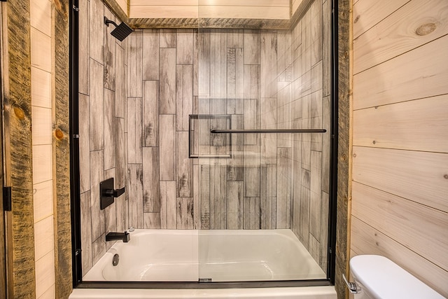 bathroom featuring shower / bathing tub combination, toilet, and wood walls