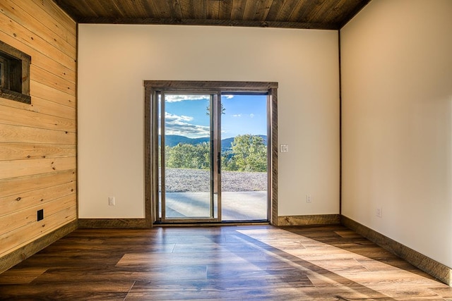 empty room featuring a mountain view, wood-type flooring, wood ceiling, and wooden walls