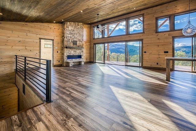 unfurnished living room with a mountain view, wooden ceiling, high vaulted ceiling, wooden walls, and a fireplace