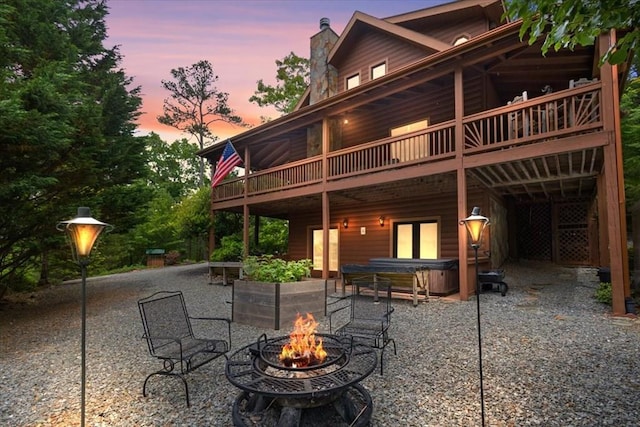 back house at dusk featuring a hot tub, a wooden deck, an outdoor fire pit, and a patio