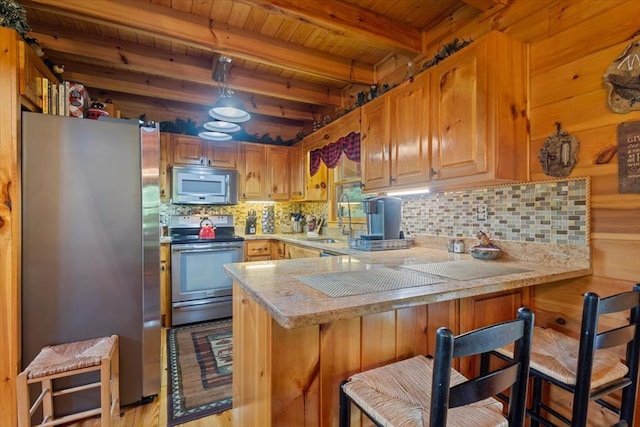 kitchen featuring beamed ceiling, a breakfast bar, kitchen peninsula, and appliances with stainless steel finishes