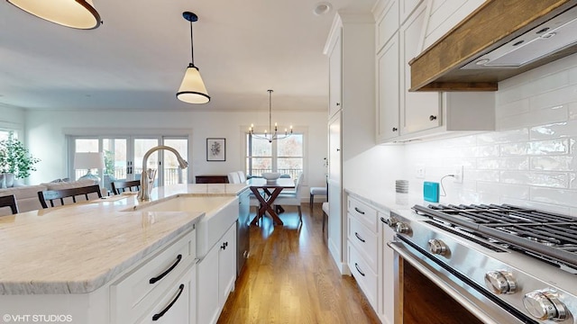 kitchen featuring custom exhaust hood, a kitchen island with sink, appliances with stainless steel finishes, decorative light fixtures, and white cabinetry