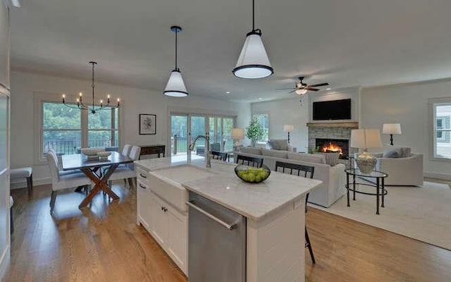 kitchen featuring a center island with sink, pendant lighting, stainless steel dishwasher, and white cabinetry