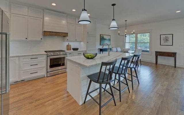 kitchen with pendant lighting, premium range hood, an island with sink, white cabinetry, and stainless steel appliances