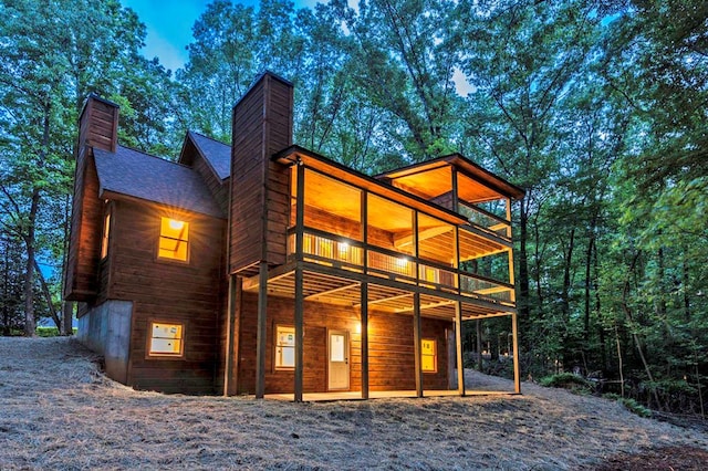 rear view of property featuring roof with shingles, a chimney, and a wooden deck