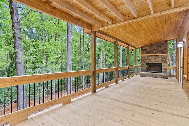 unfurnished sunroom featuring lofted ceiling, an outdoor stone fireplace, wooden ceiling, and a wooded view