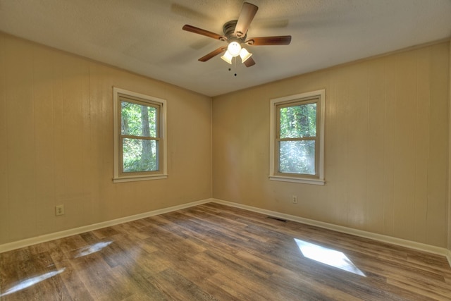 empty room featuring a ceiling fan, baseboards, visible vents, and wood finished floors