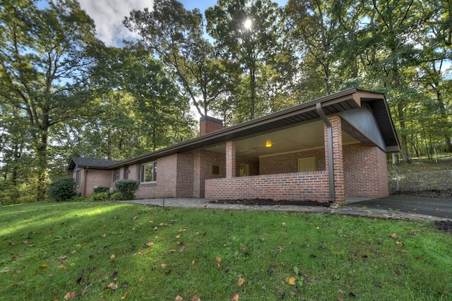 view of side of property featuring a yard, brick siding, a chimney, and fence