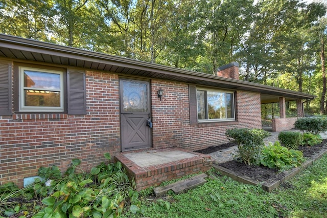 view of exterior entry with a chimney and brick siding