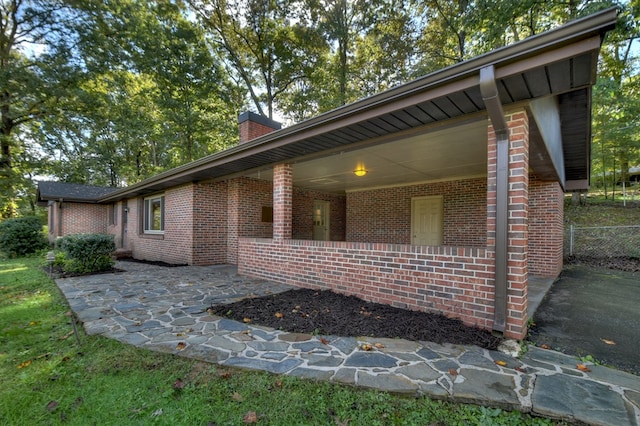 view of property exterior with brick siding, a patio, and a chimney