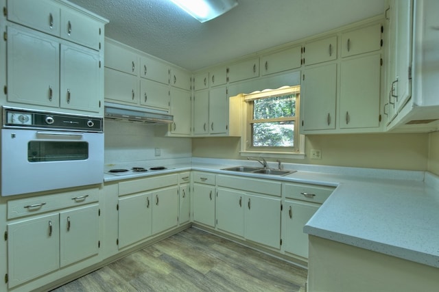 kitchen featuring light countertops, a sink, light wood-type flooring, white appliances, and under cabinet range hood