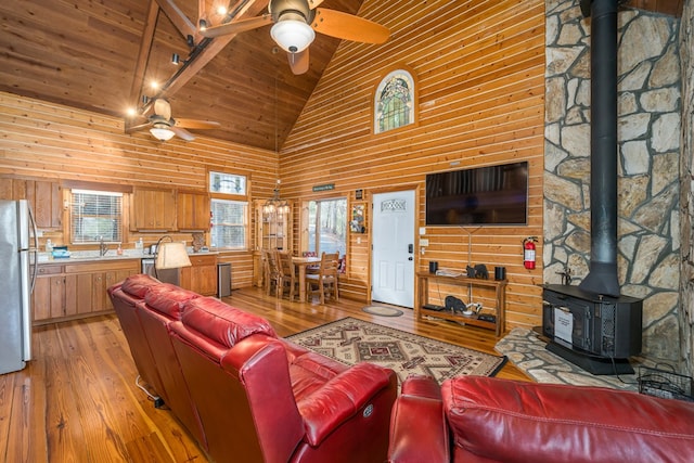 living room with high vaulted ceiling, a wood stove, sink, wooden ceiling, and light wood-type flooring