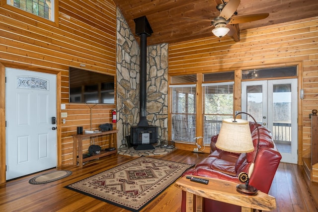 living room with dark wood-type flooring, a wood stove, ceiling fan, french doors, and wood walls