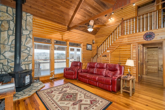 living room featuring high vaulted ceiling, a wood stove, wooden walls, beamed ceiling, and hardwood / wood-style floors