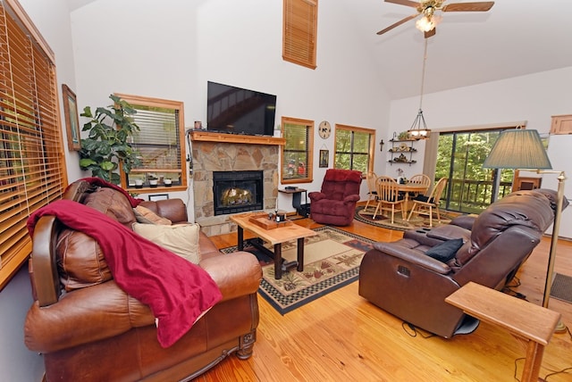 living room with high vaulted ceiling, wood-type flooring, ceiling fan, and a stone fireplace