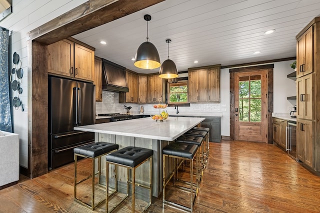 kitchen featuring stainless steel appliances, dark hardwood / wood-style floors, hanging light fixtures, a center island, and premium range hood