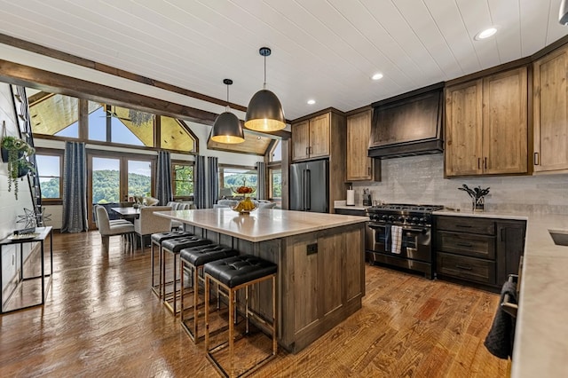 kitchen featuring wood-type flooring, high end appliances, custom range hood, a kitchen island, and decorative light fixtures