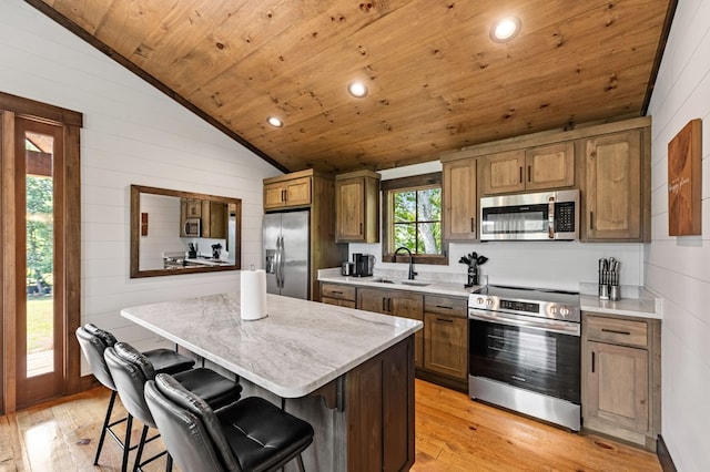 kitchen with appliances with stainless steel finishes, light hardwood / wood-style flooring, sink, a breakfast bar, and a center island