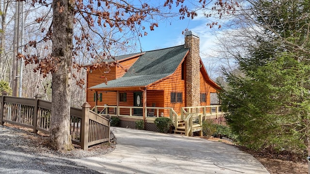 view of front facade with log veneer siding, driveway, a shingled roof, a chimney, and a deck