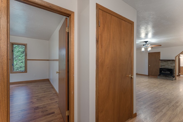 corridor with a textured ceiling, baseboards, and wood finished floors