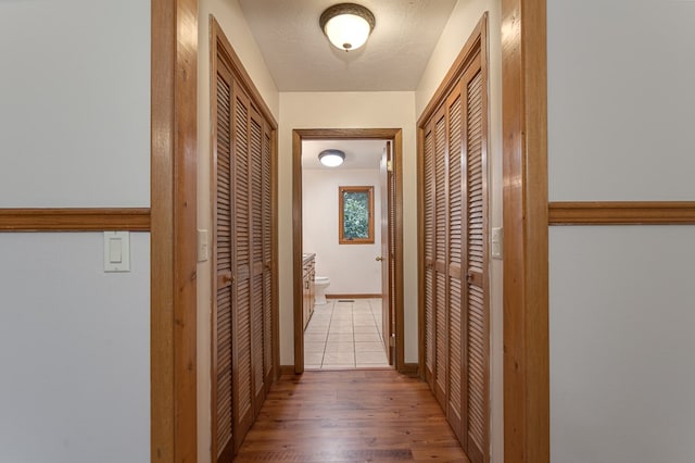 corridor featuring a textured ceiling, baseboards, and wood finished floors