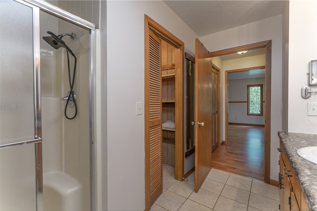 full bath with vanity, baseboards, a closet, tile patterned floors, and a stall shower