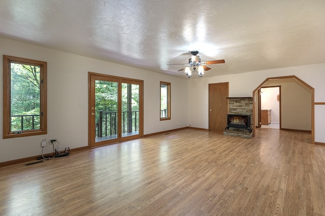 unfurnished living room with light wood finished floors, baseboards, ceiling fan, a textured ceiling, and a fireplace