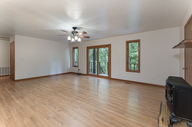 unfurnished living room with visible vents, light wood-type flooring, a wood stove, and baseboards