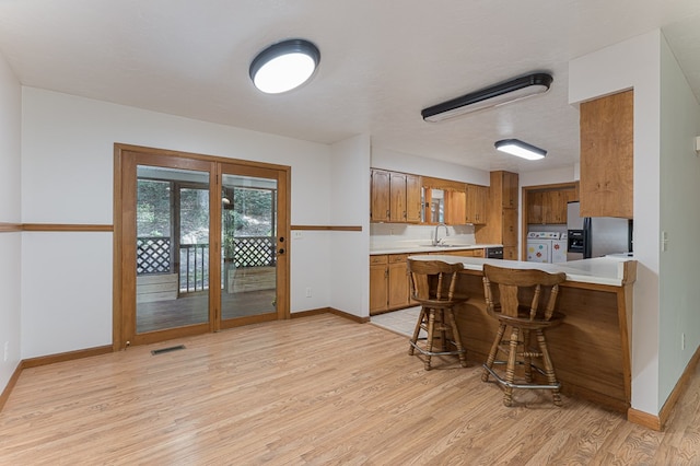 kitchen featuring stainless steel refrigerator with ice dispenser, light countertops, brown cabinetry, separate washer and dryer, and a peninsula