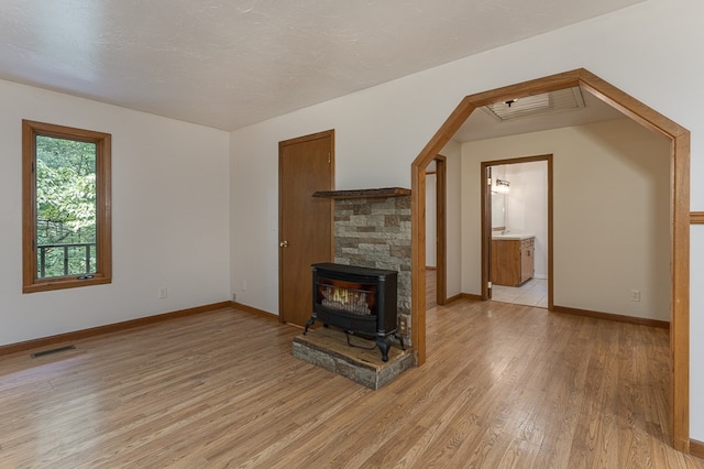 unfurnished living room featuring a wood stove, visible vents, baseboards, and light wood finished floors