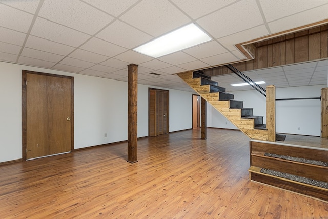 finished basement featuring a paneled ceiling, baseboards, stairway, and wood finished floors